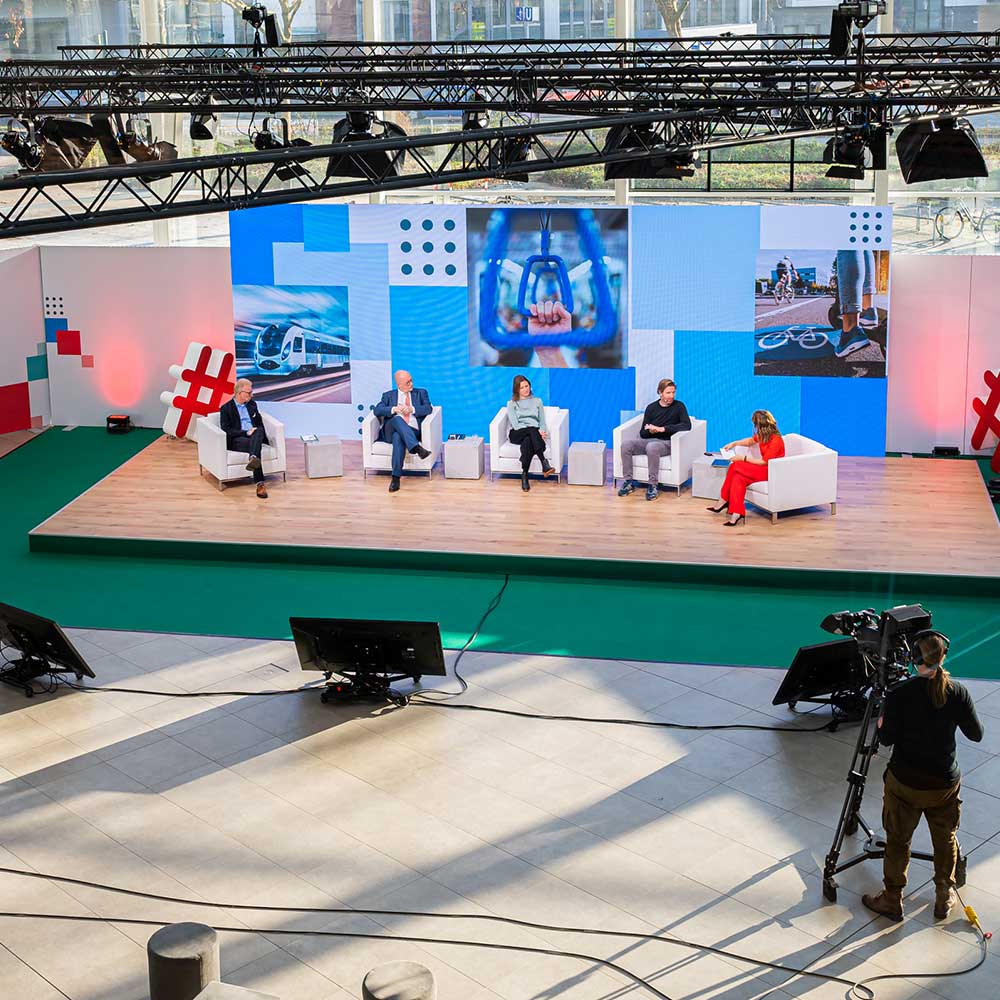 Fünf Personen sitzen auf weißen Sesseln auf einer Bühne und diskutieren miteinander.