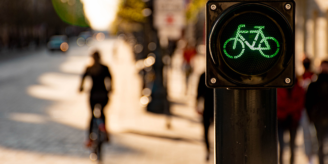 Eine Ampel zeigt ein grünes Fahrradsymbol. Im Hintergrund fährt eine Person auf einem Fahrrad über die Straße.